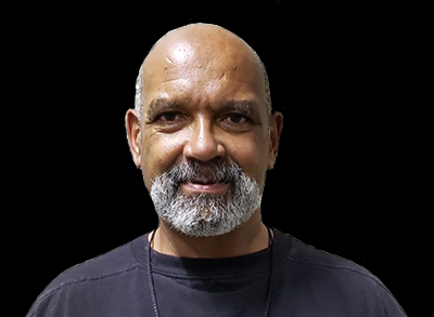Matt Nelson, A Bald Man With A Gray Beard, Smiles Slightly In A Close-Up Portrait Against A Plain Dark Background