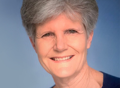 Susie Siverts Smiles Brightly Here In A Close-Up, Casual Professional Headshot Against Soft Blue Lighting Now