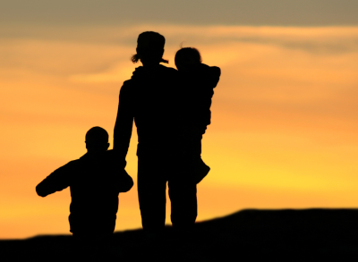 Stephanie Walking With Two Children At Sunset, One Holding Hands And One Carried, Silhouetted Against A Golden Sky