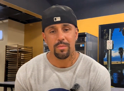 Mjames Denning, Wearing A Cap, Speaks On Camera In What Looks Like A Kitchen Or Prep Area With A Mic Visible On His Shirt