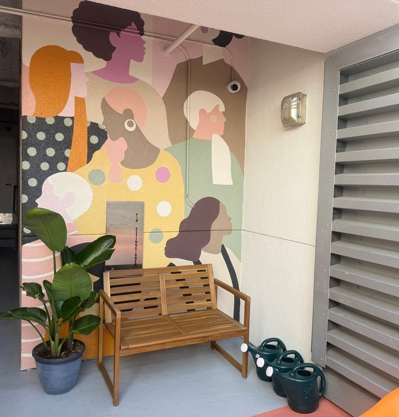 Mural of diverse faces with bench and plants at The Midnight Mission homeless services center in Los Angeles.