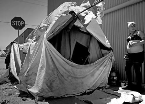 A Person Stands Beside A Tarp Shelter On A Los Angeles Street, Reflecting The Harsh Conditions Many Unhoused Individuals Face Daily