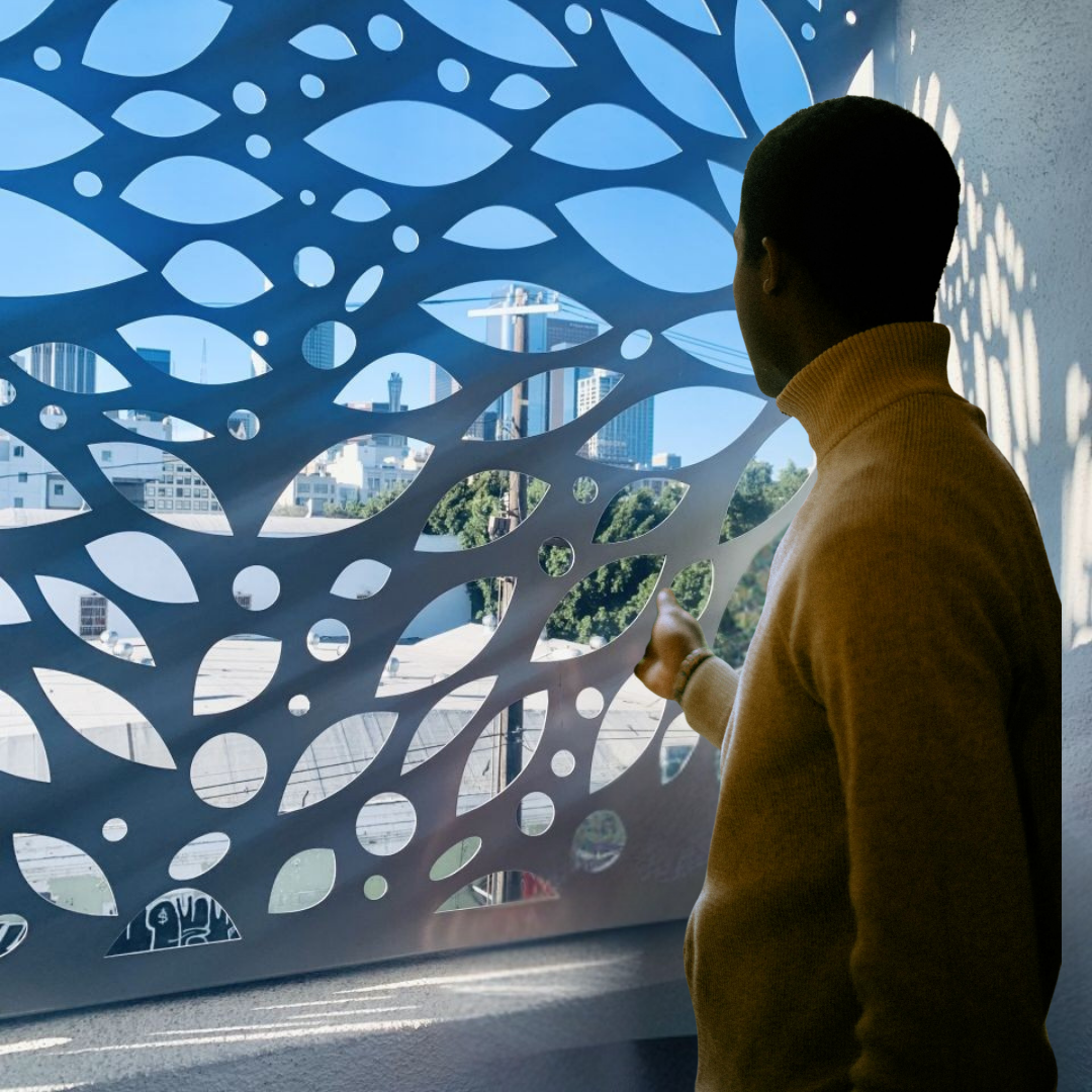 Danielle In A Turtleneck Looking Through A Decorative Leaf-Patterned Screen At The City Skyline Beyond, Bathed In Sunlight